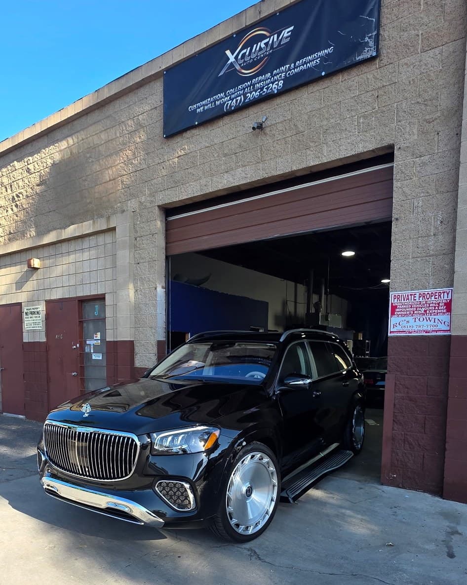 A black Mercedes-Maybach GLS parked in front of Xclusive's building beneath the shop's banner, beside its open bay door