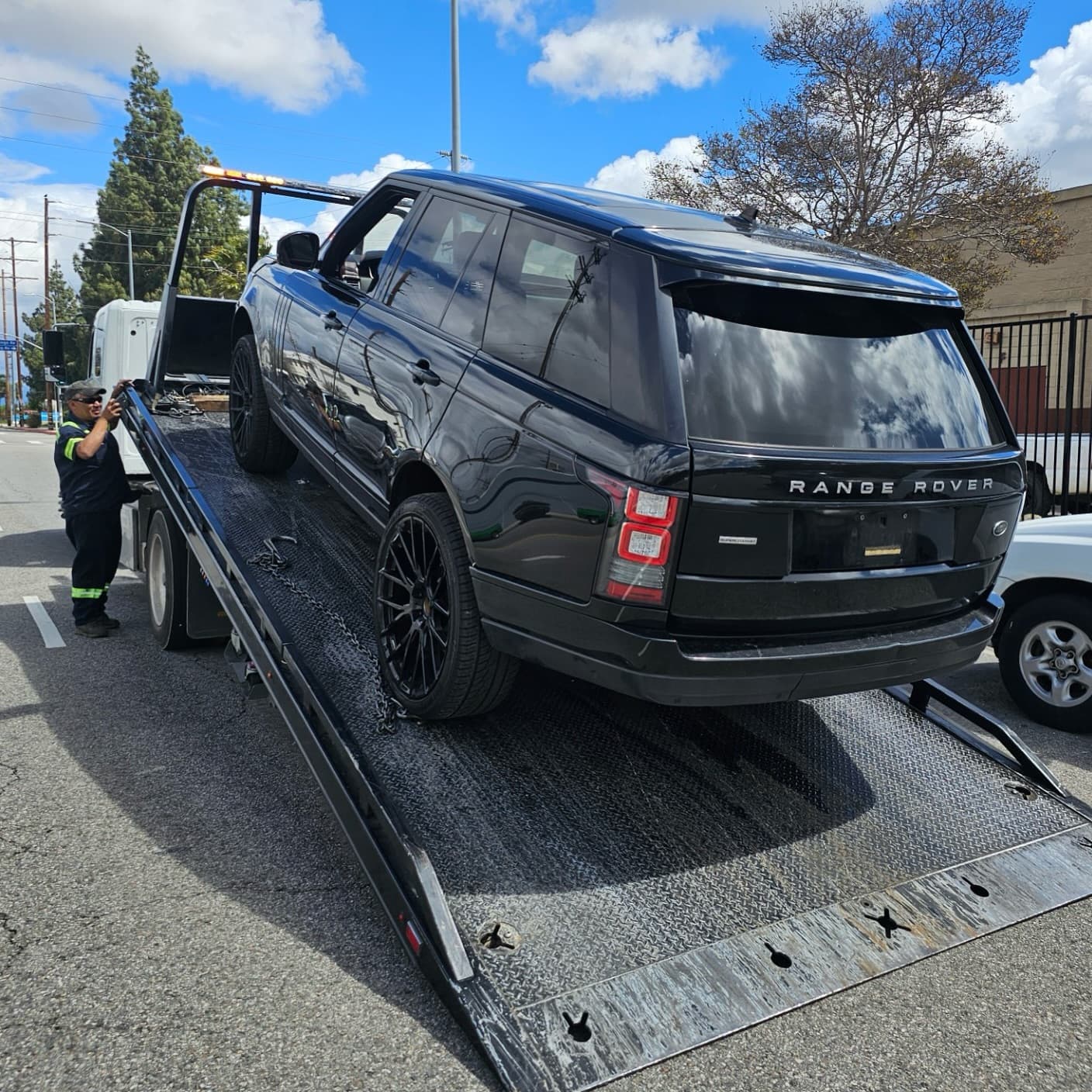 A tow operator loading a customer's black Range Rover onto a flatbed truck outside, the first step after an accident