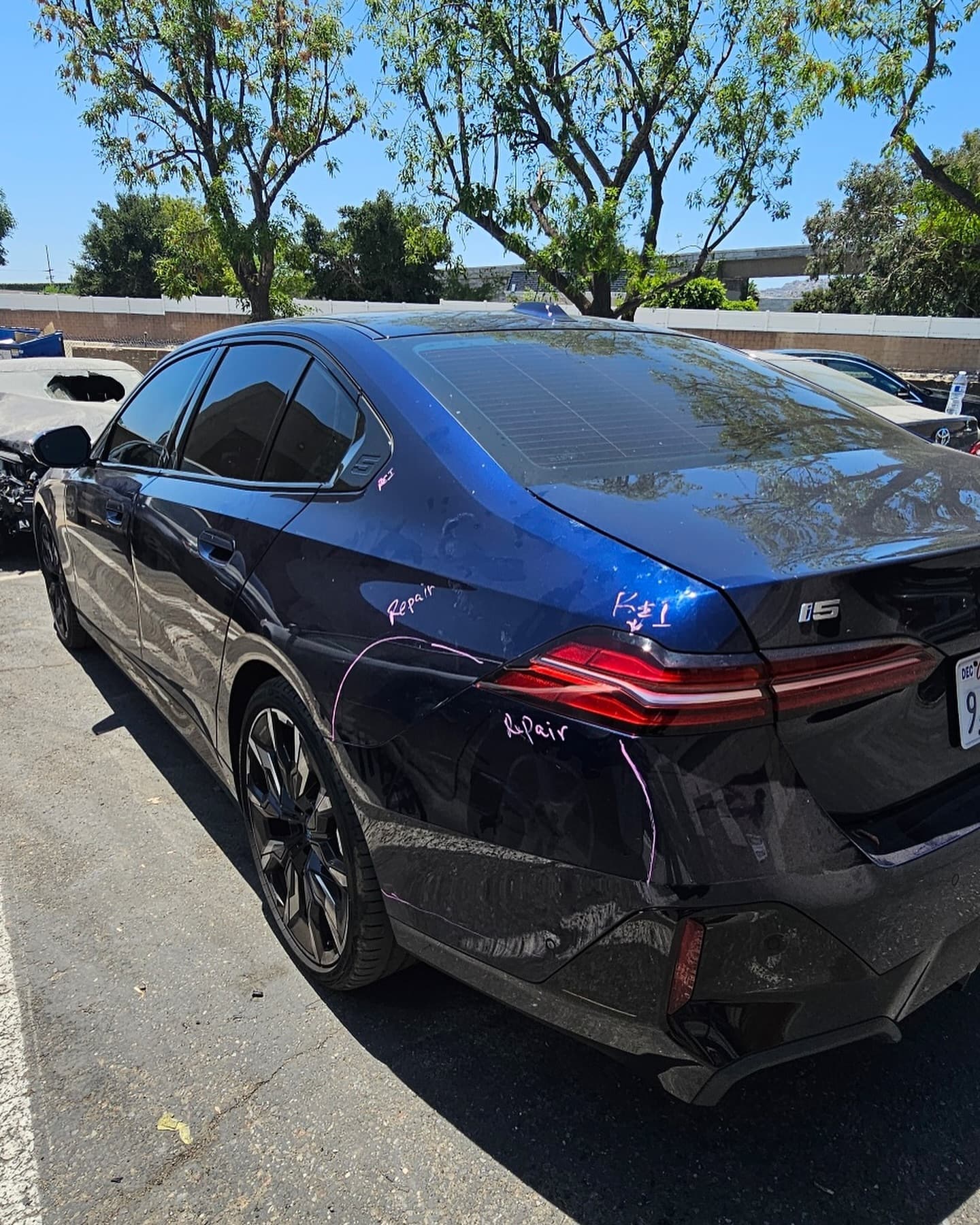 A deep-blue BMW i5 at the shop, dents on the rear door and quarter panel circled in grease pencil and marked for repair
